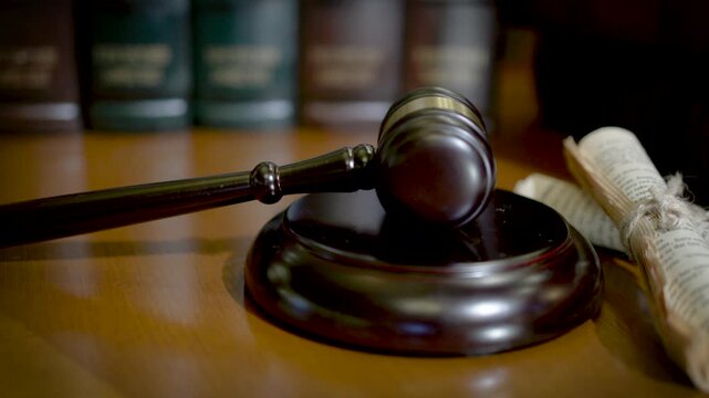 A top-down view of a wooden judge's gavel and sound block placed on a dark wooden surface with rich warm tones.
