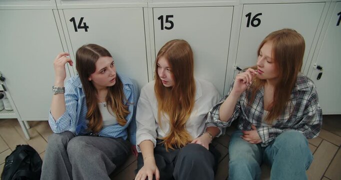 Three teenage girls having private conversation by school lockers