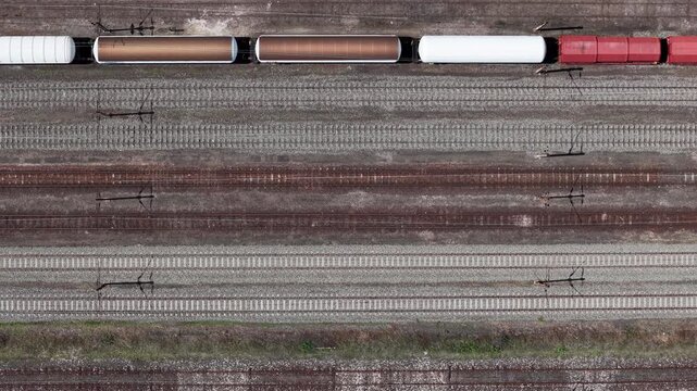 An aerial top-down perspective displays freight train carriages and tanker cars stationed along parallel industrial railway tracks in rural Hungary.