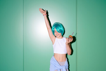 Fototapeta premium Joyful young girl with bright blue wig and cupcake celebrates her birthday with a happy dance and