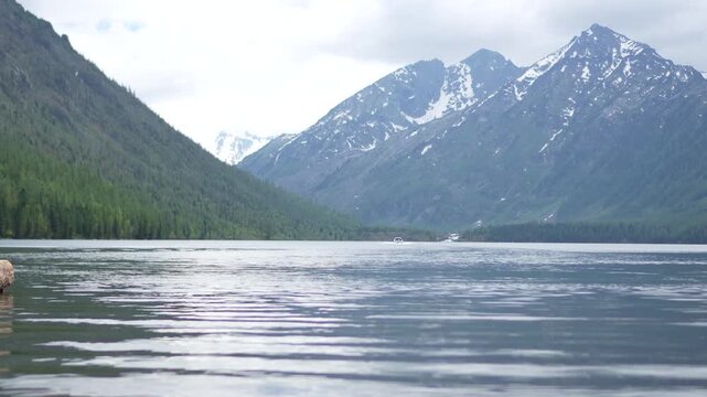 A cinematic focus pulling shot starting from close-up ripples on a pristine alpine lake surface and refocusing on distant cloudy mountain valleys in Altai.