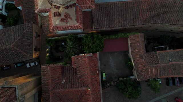Top down drone view of a medieval church and cloister complex with stone courtyard surrounded by terracotta rooftops in historic Spain.