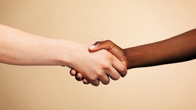 Close-up of two hands shaking against a neutral background.