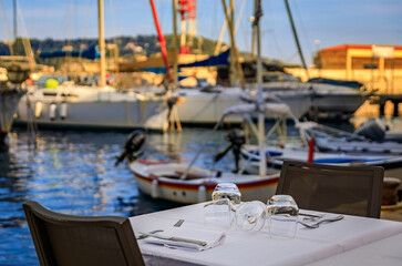 Fototapeta premium A table at an outdoor restaurant with a view of boats in the marina on the Mediterranean Sea in old town of Villefranche sur Mer, South of France