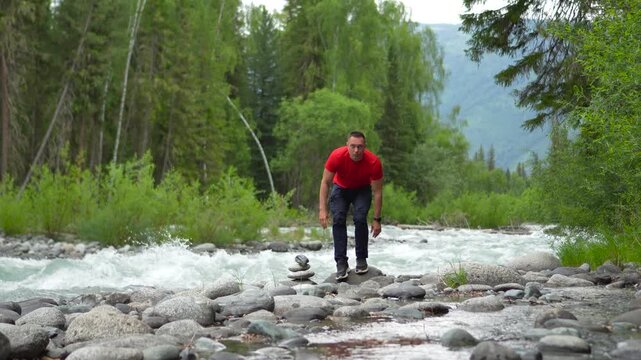 A man is traveling through the Altai Mountains. A man in red is meditating and practicing breathing exercises on the banks of a mighty mountain river. He sits in the lotus position on the riverbank, f