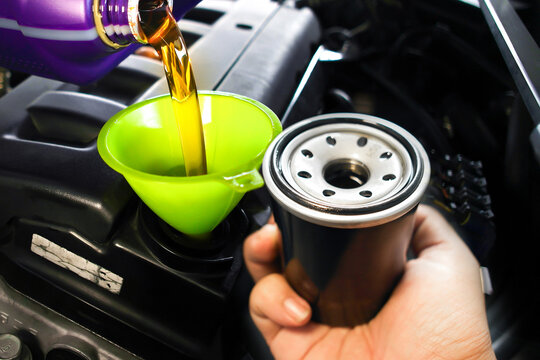  Pouring fresh motor oil through a green funnel into the car engine during an oil change service with a new oil filter