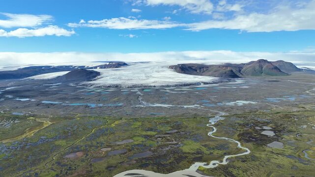 Aerial view of the vast Hofsjokull glacier with its icy expanse, rugged dark volcanic terrain, and winding glacial rivers flowing through the landscape in Blonduos, Hunabyggd, Iceland.
