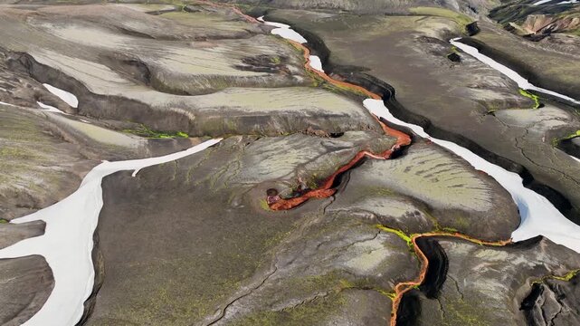 Aerial view of the volcanic landscape of Raudufossafjoll with dark lava fields, winding river channels, and patches of snow in Kirkjubaejarklaustur, Skaftarhreppur, Iceland.