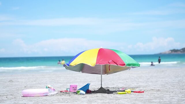 Beach umbrella on sand by ocean under bright sky, summer vacation travel seascape with colorful parasol shading toy bucket and inflatable ring, calm waves, blue horizon, leisure day