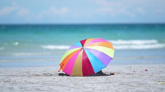 Colorful beach umbrella parasol on sand shore by ocean, seascape coastline with gentle wave, turquoise water blue sky, relaxing holiday mood, summer travel vacation background, copy space