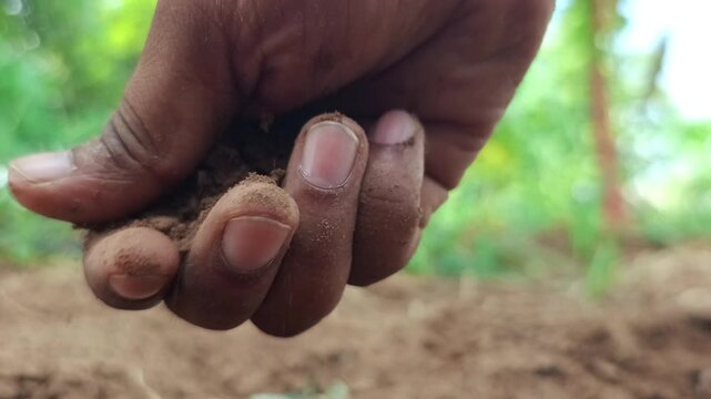 Extreme close up of a farmer hand squeezing and pouring fertile brown soil on the ground