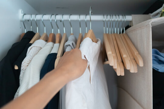A person's hand selecting a white shirt from a neatly organized wardrobe clothes rack.