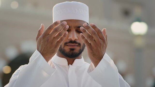 Devoted Muslim man subtly moving open hands in prayer, eyes closed, reflecting spiritual devotion in Makkah