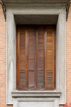 A vintage wooden window with louvered shutters set into a brick facade and concrete frame, evoking rustic, cozy architecture and classic urban detail suitable for design, restoration, and lifestyle