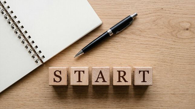 Wooden blocks spelling out START next to a notebook and pen