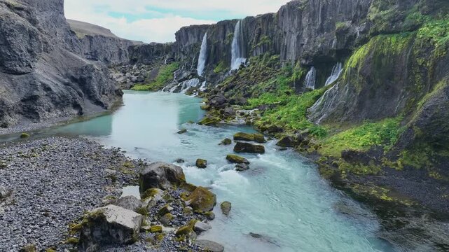 Aerial view of Sigoldugljufur canyon with multiple waterfalls cascading over mossy volcanic cliffs into a turquoise river in Hella, Rangarthing ytra, Iceland.