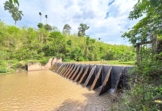 Water cascading through a series of concrete inclined buttress fins on a river weir dam. Built to stabilize riverbed levels, store agricultural water, and control stream flow in a countryside envir