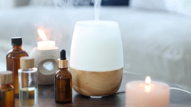 Modern aroma lamp, burning candles and bottles of essential oils on table indoors, closeup. Camera moving forward