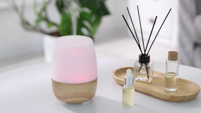 Aromatherapy. Modern aroma lamp, reed diffuser and bottles of essential oils on light table indoors, closeup. Camera moving forward