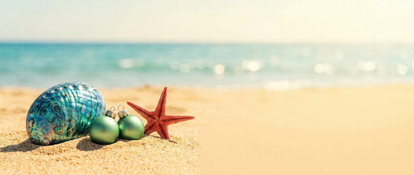 Tropical Christmas banner with iridescent paua shell, christmas baubles and starfish on sandy beach, southern hemisphere holiday concept. 