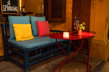 Fotobehang Horeca Cozy cafe corner with colorful pillows on a bench, candle and flowers on a small red table.  © Max