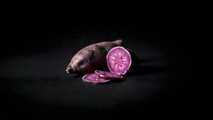 Obraz premium Sliced purple sweet potato on black surface – Ideal for exotic root vegetable promotions, vegan meal kits, or gourmet food photography.