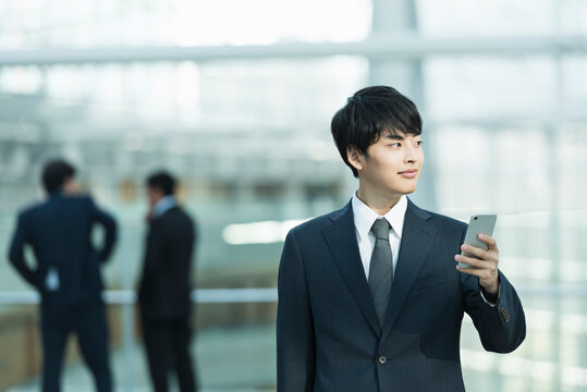 オフィスビルのロビーでスマートフォンを操作する20代男性ビジネスマン