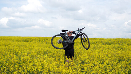 Fototapeta premium Moments of cycling. A man poses with his bicycle in a rapeseed field; a male athlete holds his bicycle behind his head, enjoying the views of the yellow rapeseed field.