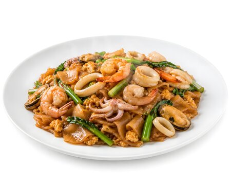 Stir-fried wide rice noodles with seafood in soy sauce, a Thai dish, served on a white plate against a white background, ready to eat.