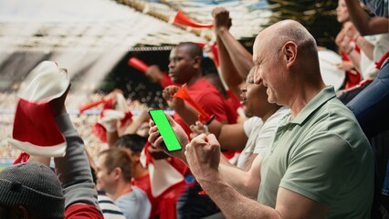 Naklejka premium Vertical chroma key phone screen with football fan during soccer match in a packed stadium crowd, Supporters chanting and cheering for the red team, authentic live football match culture.