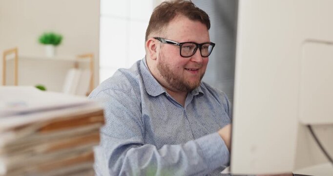 Happy overweight man accountant smiling in office. He works at a computer on analysis, reviewing spreadsheets with calculator during audit and budget. Clear concept of finance success.
