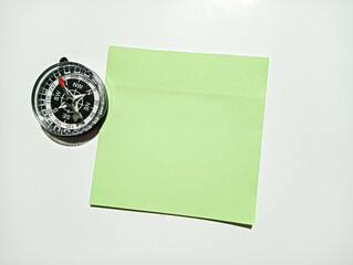 Blank green sticky note beside a compass on a white background. Minimal concept for planning, direction, navigation, goals, reminders, business strategy, and copy space. © Gabie