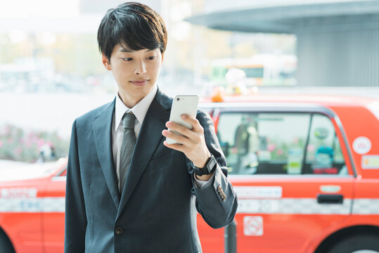 東京駅前でスマートフォンを操作する20代男性ビジネスマン