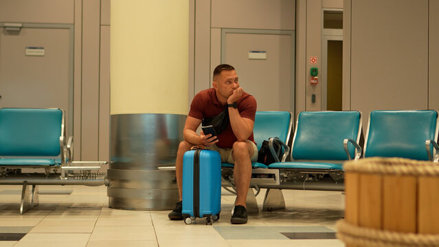 Air travel. A tired man waits at the airport for his delayed flight. The man is nervous and awaits the boarding call.