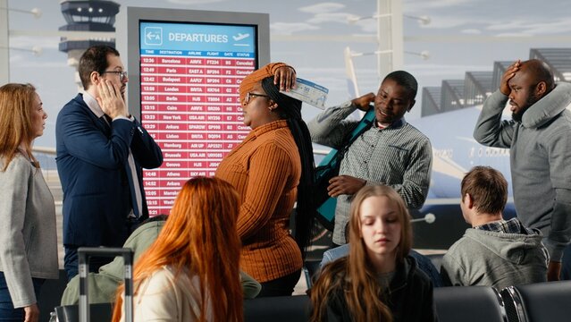 Dejected by plane being late, FIDS screen and upset men with women in airport checking departure time, tedious waiting, electronic timetable display announcement and passengers bummed by flight delay.