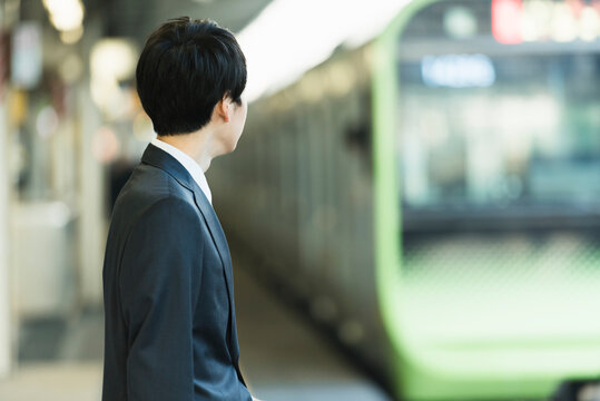 駅のホームで電車を待つビジネスマンの後ろ姿