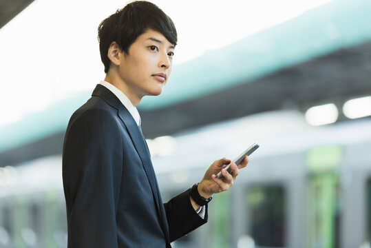 駅のホームでスマートフォンを操作する20代男性ビジネスマン