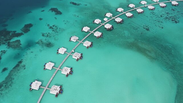 Aerial view of luxury overwater bungalows connected by a wooden walkway over the turquoise lagoon in Kudahuvadhoo, Dhaalu Atoll, Maldives.