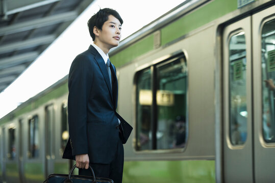 駅のホームで電車を待つ20代男性ビジネスマン