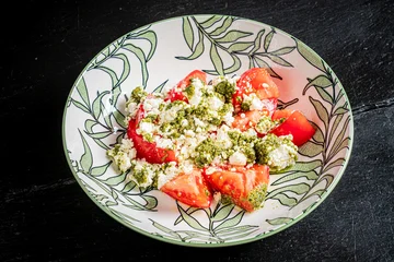 Fresh tomatoes topped with creamy cheese and vibrant green pesto for a delightful summer dish © Maksim Shebeko