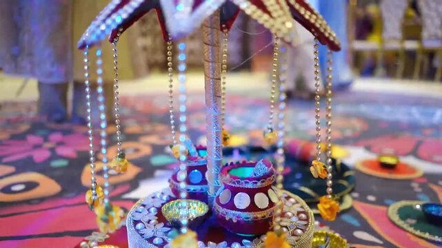 Close-up footage of a traditional Mehndi ceremony centerpiece featuring decorative hanging ornaments, colorful lighting, and handcrafted wedding decor. 