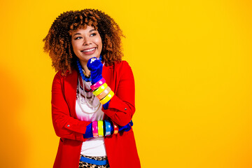 Smiling young woman in colorful fashion with curly hair and bold accessories against a bright...