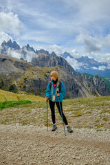 Obraz premium Woman hiking in the Dolomites mountains during a bright day with stunning peaks and clouds