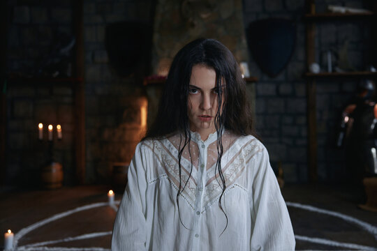Woman practitioner in medieval chamber surrounded by candles and ancient artifacts