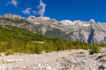 Fototapeta premium Mountain landscape in the Albanian Alps near Theth, Albania. Theth Valbona valley trek Peaks of the Balkans scenic way. Rugged peaks rise above forested valleys and alpine meadows
