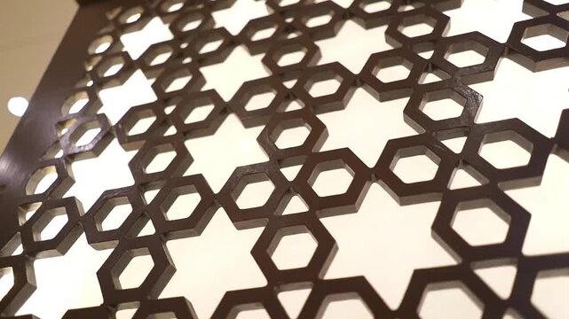 Close-up footage of an elegant wooden geometric decorative panel with soft backlighting. Modern interior design element featuring intricate lattice patterns, architectural details, 