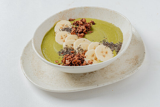 Delicious green smoothie bowl topped with fresh banana slices and crunchy granola