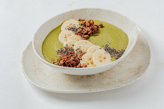 Delicious green smoothie bowl topped with fresh banana slices and crunchy granola