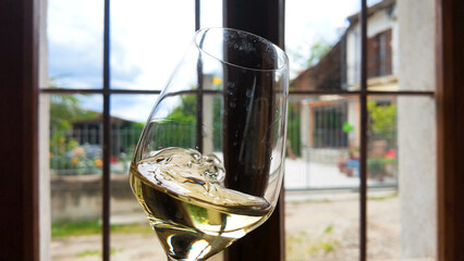 Fototapeta premium White Wine Swirling in Glass Before a Rustic Italian Window