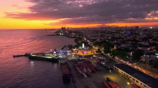 Cinematic aerial drone footage capturing the Fray Ant&oacute;n de Montesinos monument at sunset, overlooking the Caribbean Sea, the port, and the vibrant cityscape of Santo Domingo